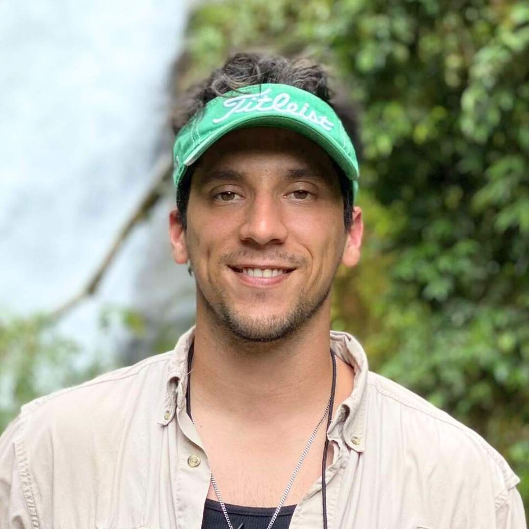 A man with a smile is wearing a green hat while outdoors.