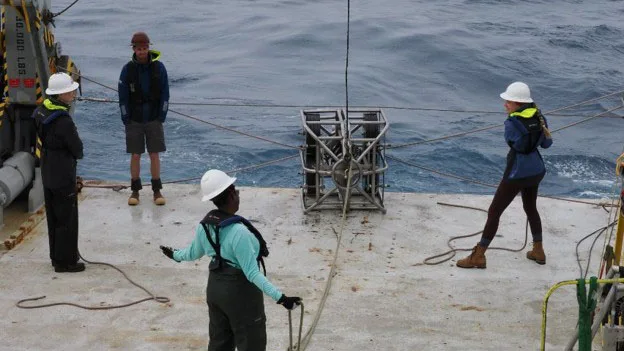 Researchers get ready to lower a deep sea measurement instrument into the water.