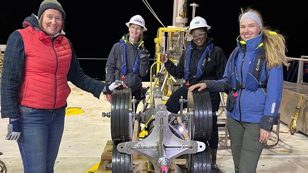 A group of research scientists dressed in winter clothes standing around an instrument on a research vessel at night.